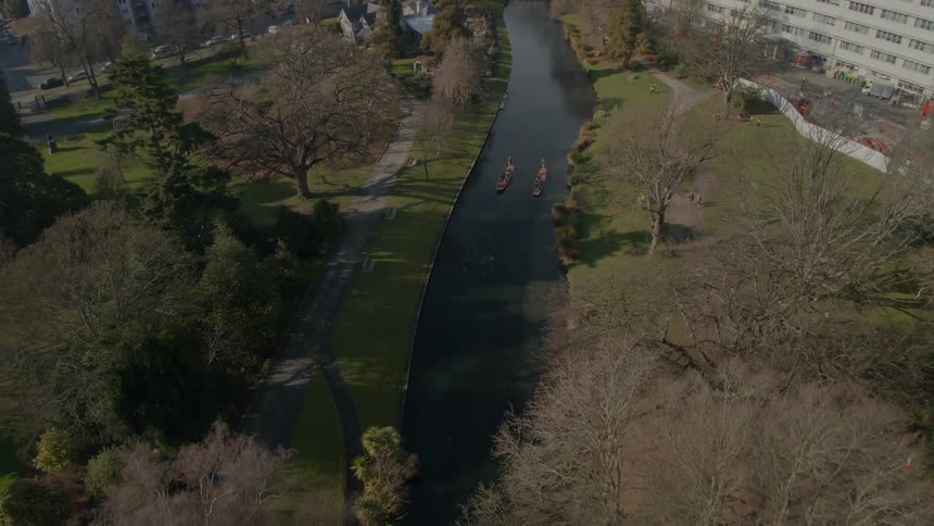 Two boats full of people sail down a narrow river that runs though a city park