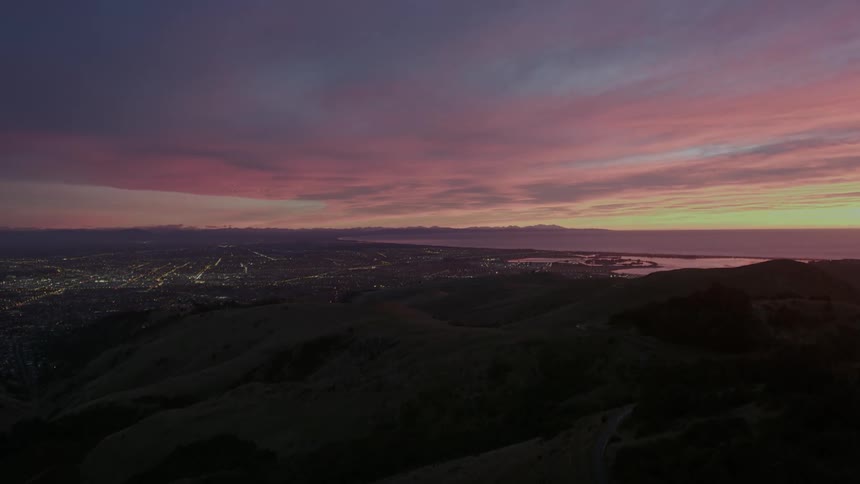 Bright lights light up a city neighborhood below rolling hills