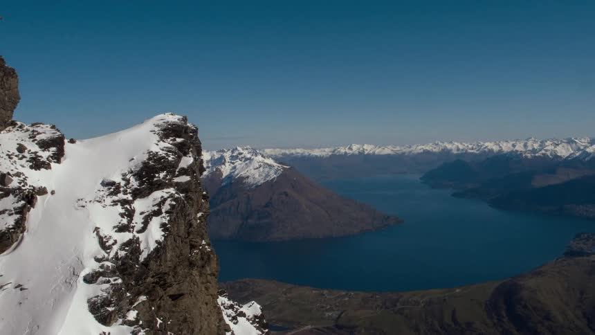 Snow tops the peaks of a mountain range overlooking a lake