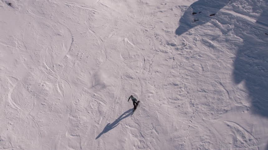 A man pumps his fist while looking at a mountain lake view then turns and snowboards down the slope