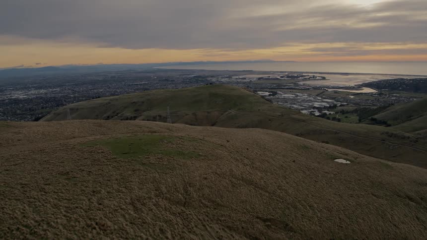 Traveling over the top of a grass covered hill with a rural area on the other side and a lake in the distance