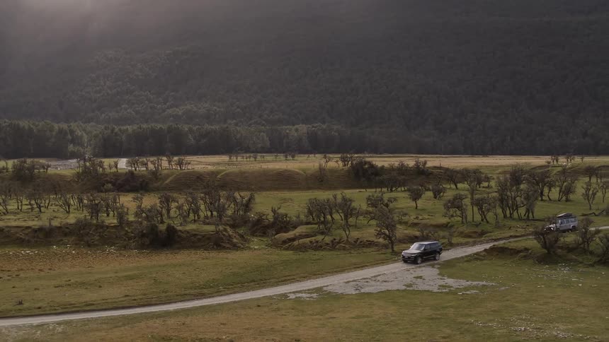 A pair of vehicles travel along a road through a vast countryside during the day