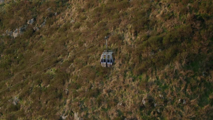 A gondola lift descends a mountain during the day