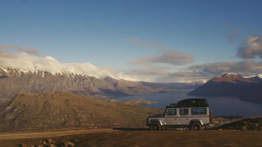 A jeep style vehicle travels a mountain pathway beside a lake