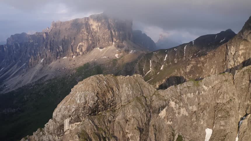 Low lying clouds touch tops of snow accented rocky craggy steep mountains surrounding green valley