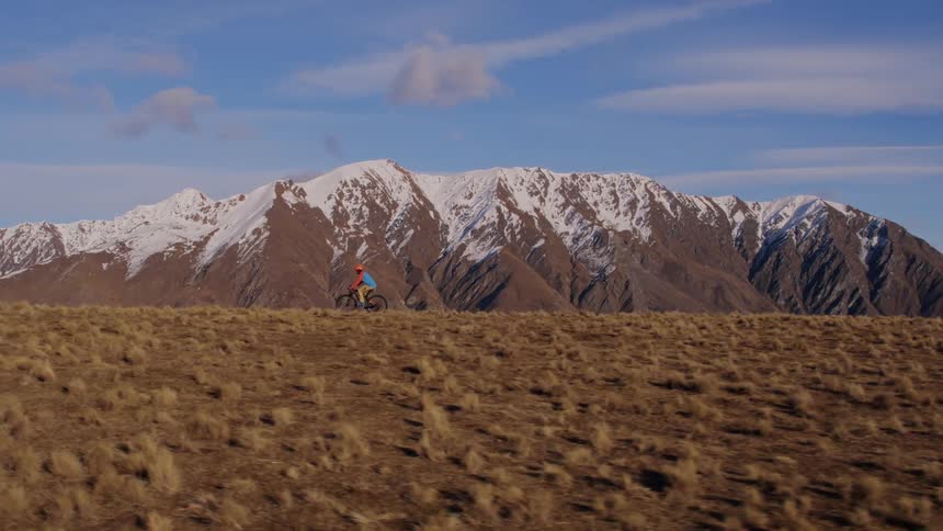 A mountain range has its peaks covered in a blanket of snow while the valley below is dry and dead