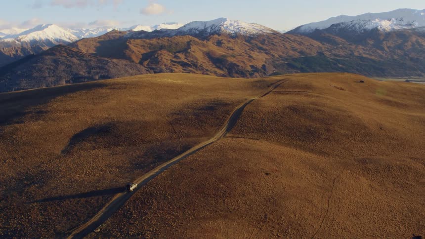 A van is traveling on a rural road with snow covered mountains in the distance