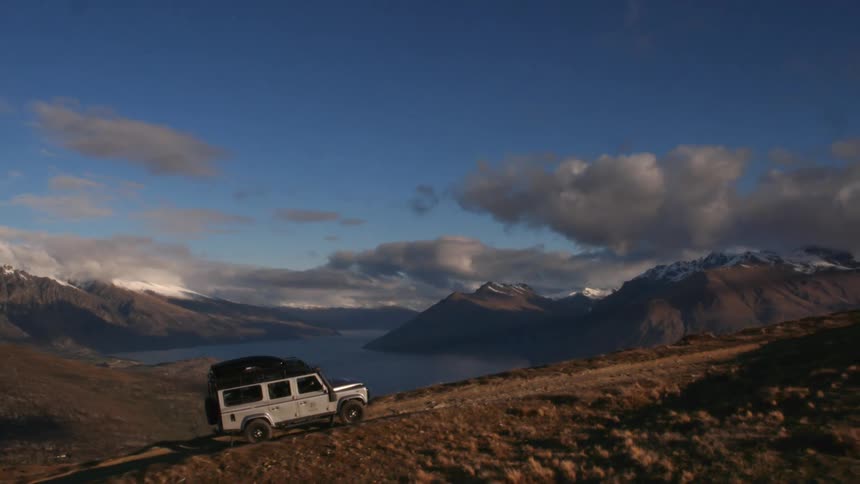 A jeep style vehicle climbs a mountain trail beside a lake