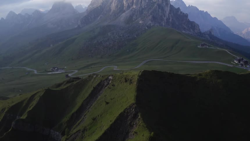 A road winds throughthe hills beneath tall rocky peaks