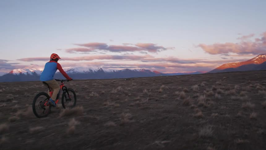 Man rides a bicycle over a field towards the snowy mountains