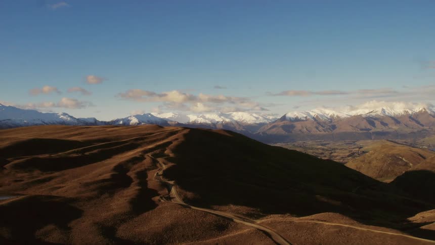 A landscape with hills with a mountain range the sky and clouds in the background