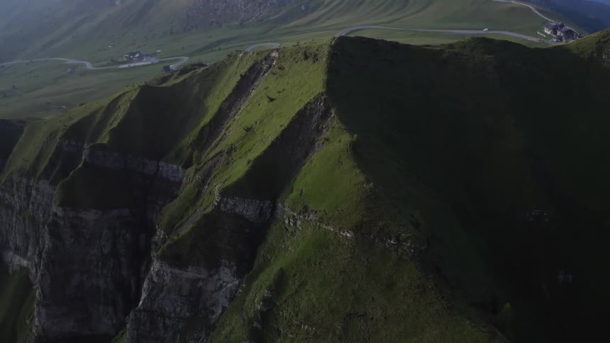 Grass covered hills and a mountain range with peaks high in the clouds