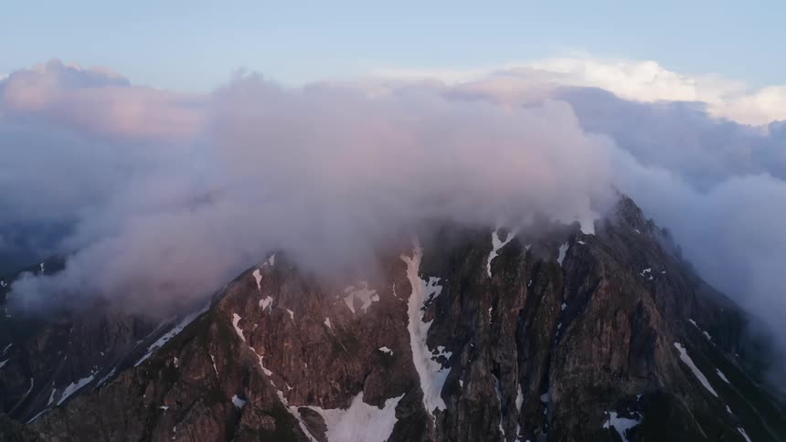 Aerial view of a mountain peak covered with streaks of snow under the clouds