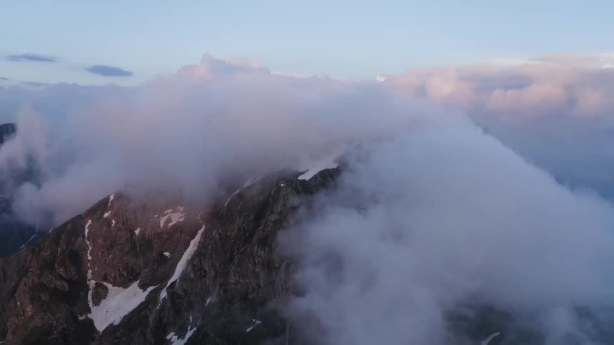 A mountain range with snow and ice surrounded by clouds with the sky in the background