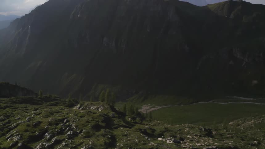 Grass covered rocky terrain with a huge cliff and a mountain range on the other side