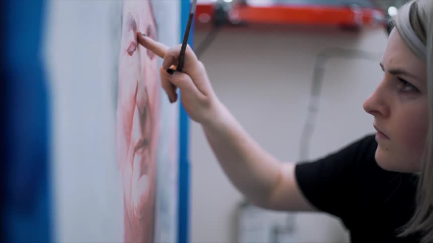 A woman paints on the canvas before her
