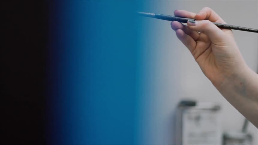 A hand holds a paintbrush close by a painting