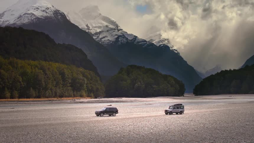 Two cars are driving in a remote area near mountains