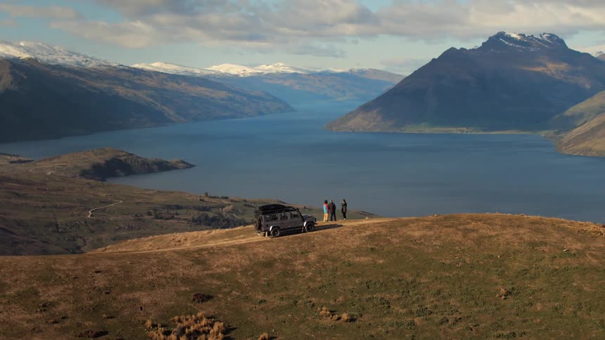 A group of people stand near their vehicle on the mountain