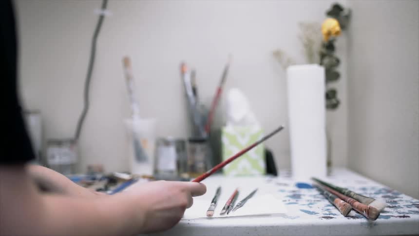 A person dabs a paintbrush on a piece of white paper