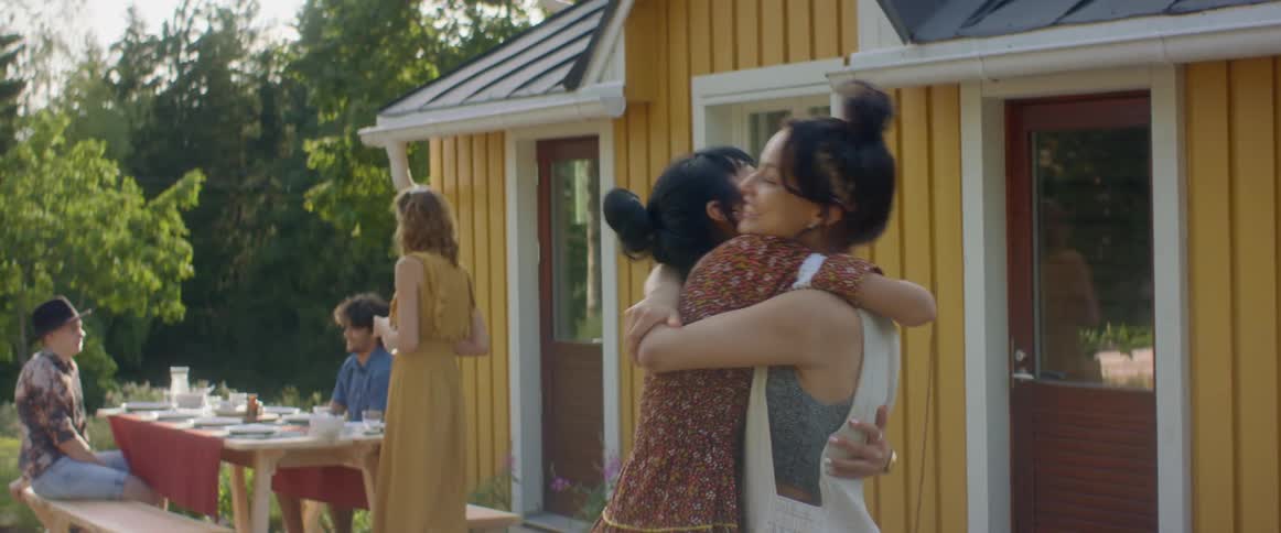 Two woman hug and greet each other happily at an outside gathering
