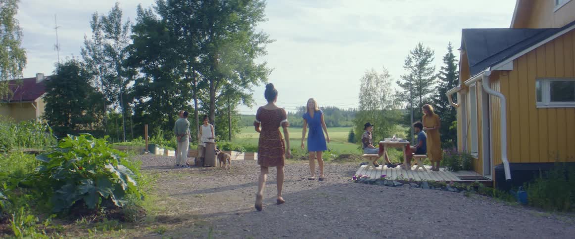 A woman walks in a yard and greets a woman with a hug