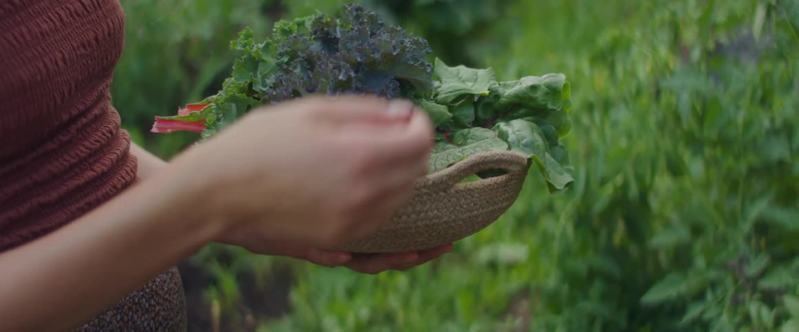 A woman standing outside places berries in a basket of fresh herbs