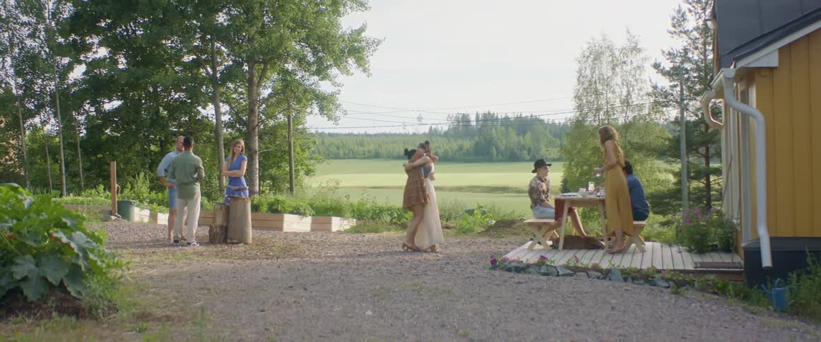 Two women walk towards each other and embrace at a backyard party with friends
