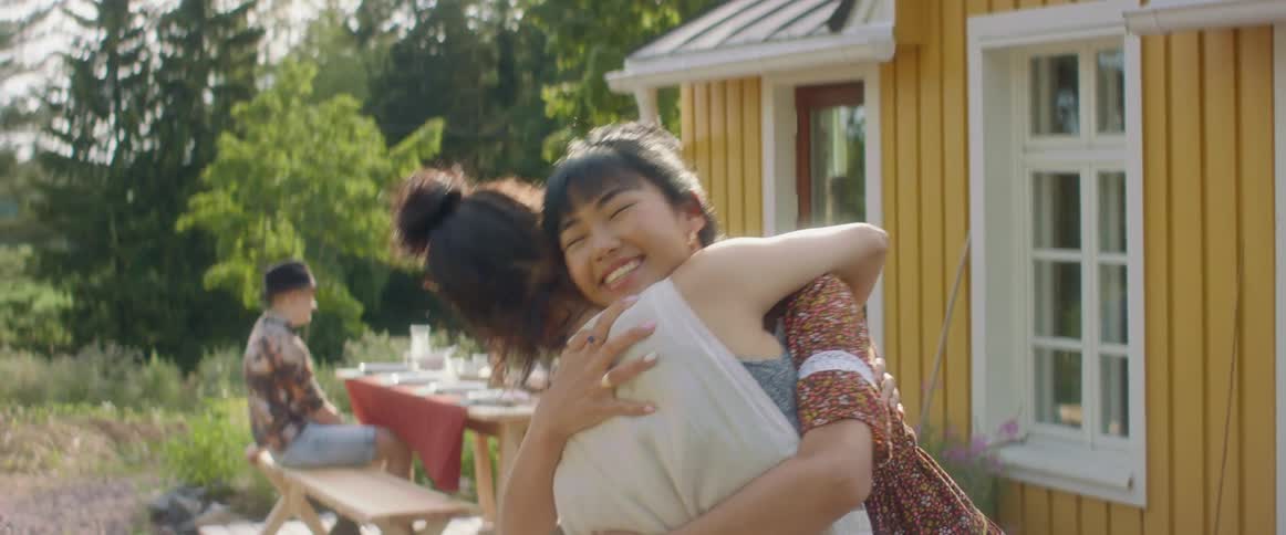 A pair of women greet each other with a hug outside of a house during the day