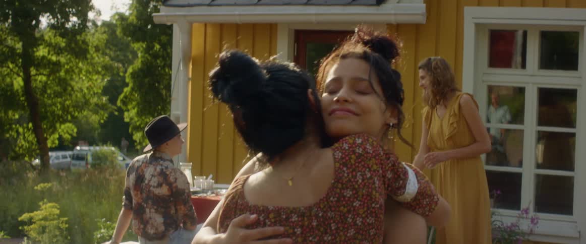 A pair of women greet each other with a hug at an outdoor meal