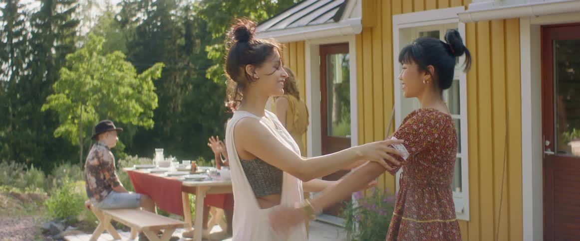 Woman greets female friend as other friends congregate around picnic table