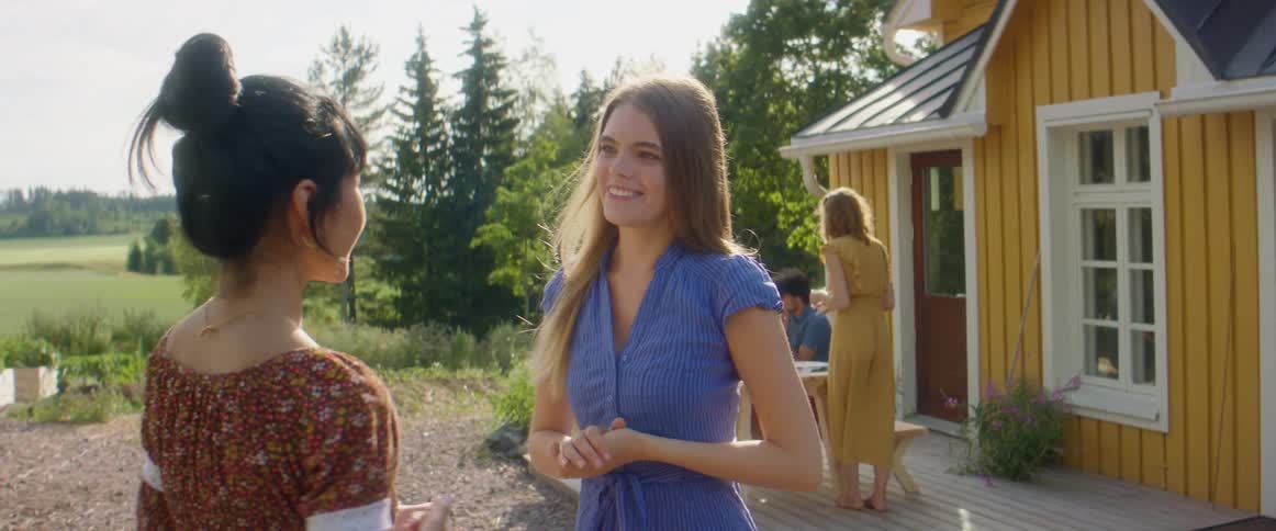 A pair of young women greet each other with a hug before beginning to chat outdoors during the day