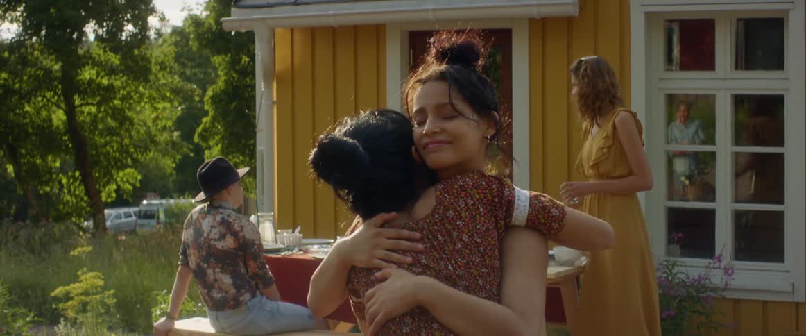 Two young women greeting each other and hugging at an outdoor gathering