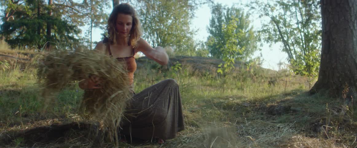 A woman kneels in the forest and lays hay on the ground