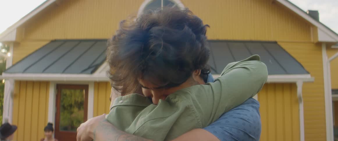 Friends cuddle each other in front of yellow house