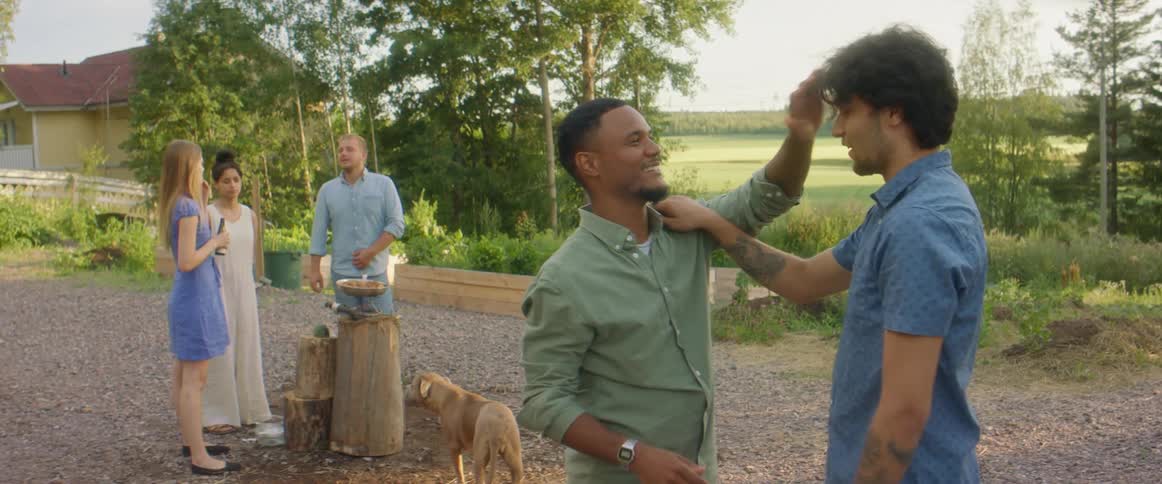 Two men laugh and hug while two women and another man and a dog stand behind them