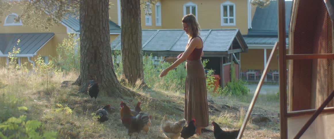 A woman in a long skirt feeding chickens on a farm in summer