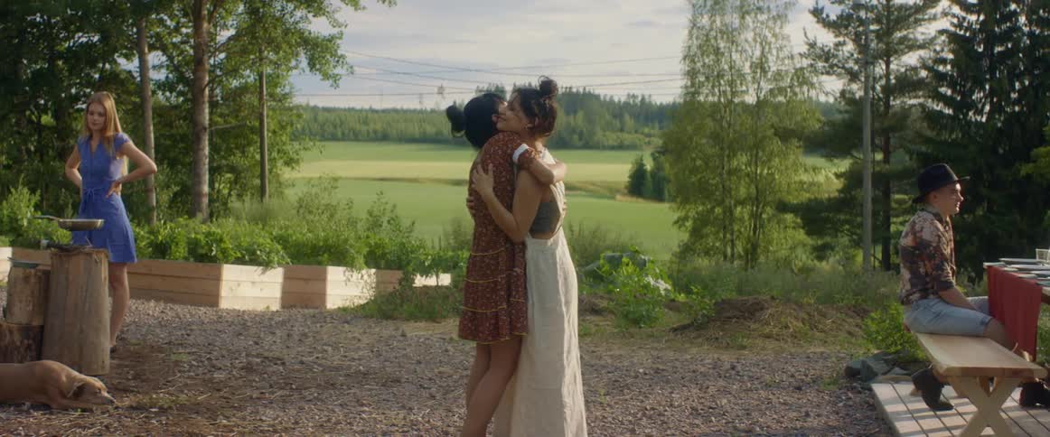 Two women hugging with trees the sky and clouds in the background