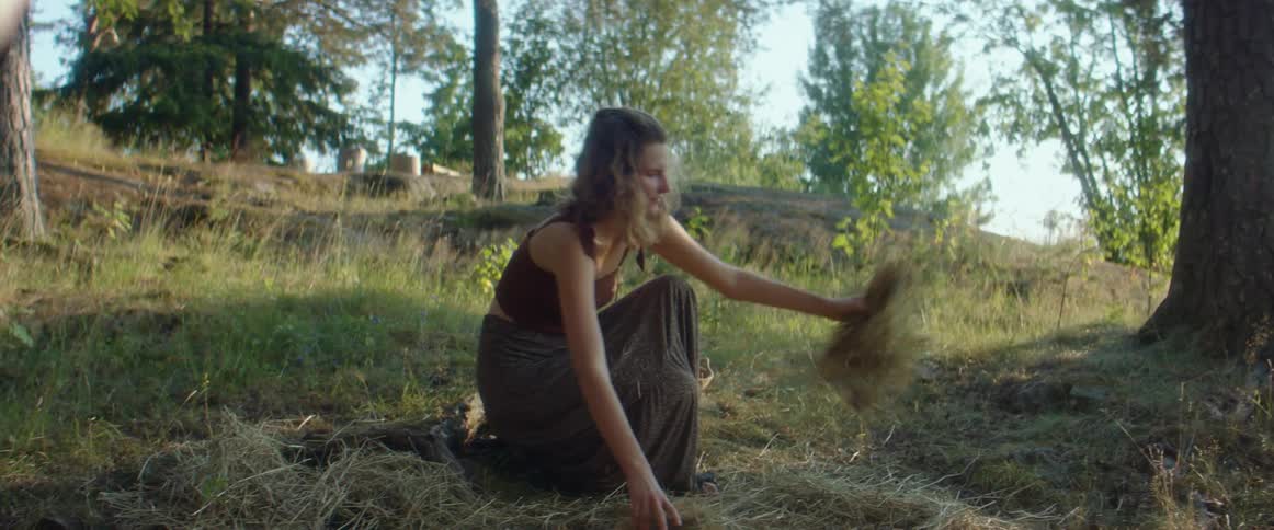 Woman wearing skirt and short camisole top spreads straw along sloping ground