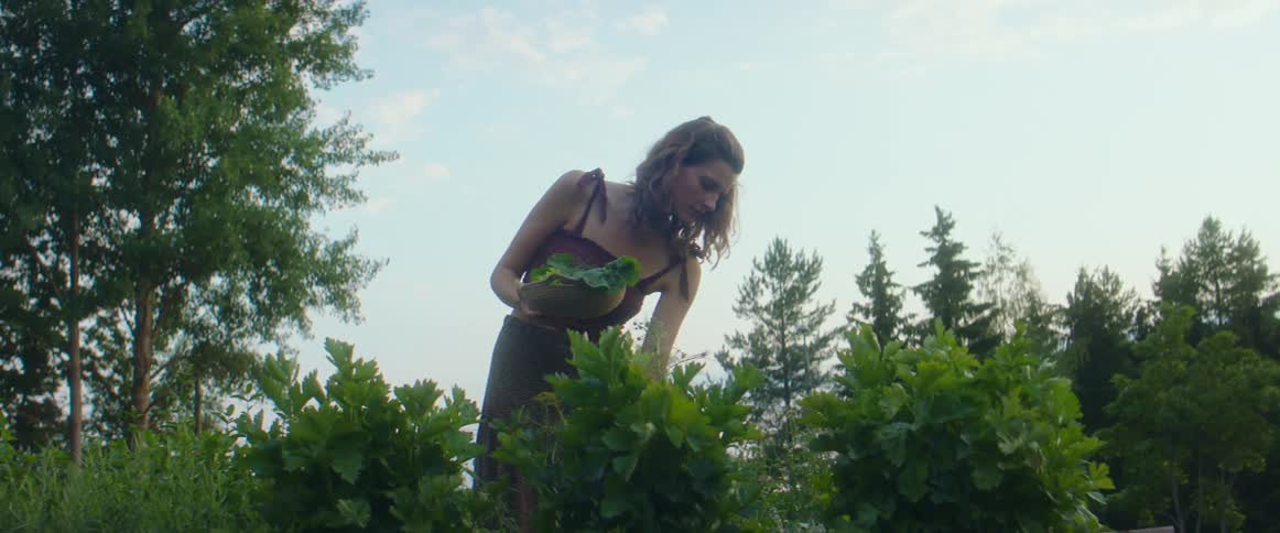 A woman picking leaves off of a plant outdoors