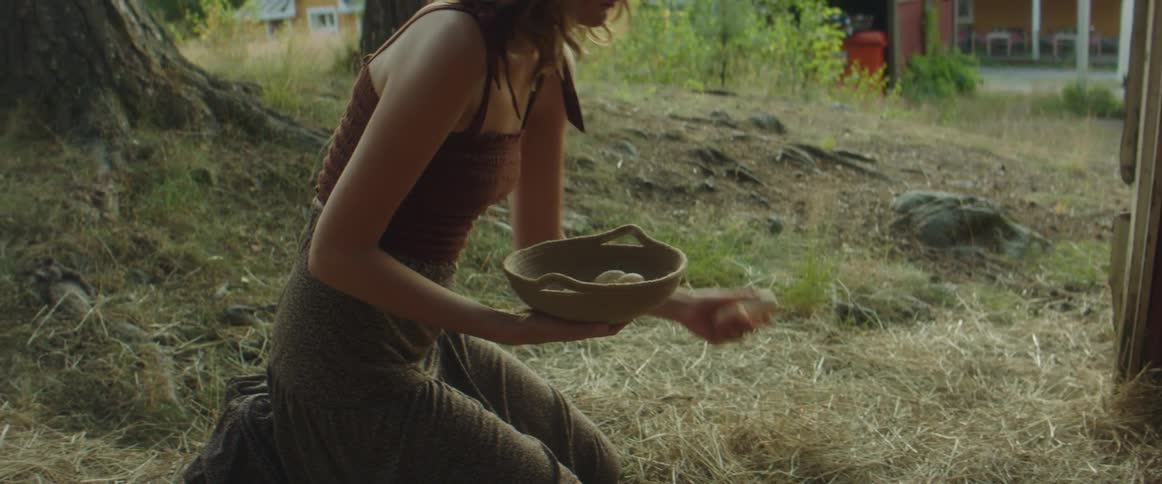 A woman kneeling and gathering chicken eggs from hay on the ground