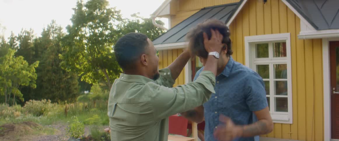 Two men talking and hugging with people sitting at a picnic table in the background