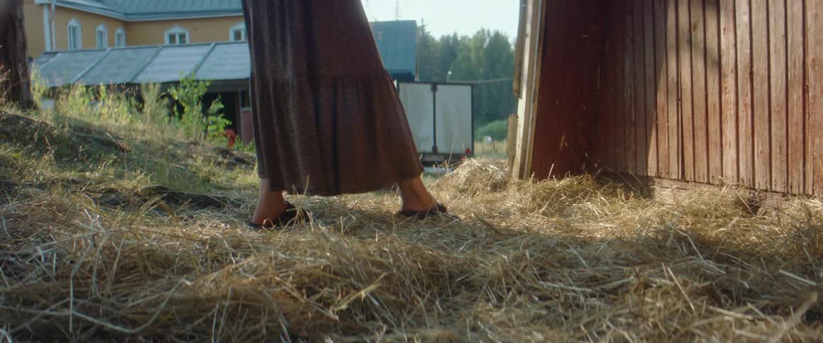 A woman stands outside of a barn with falling hay beside her