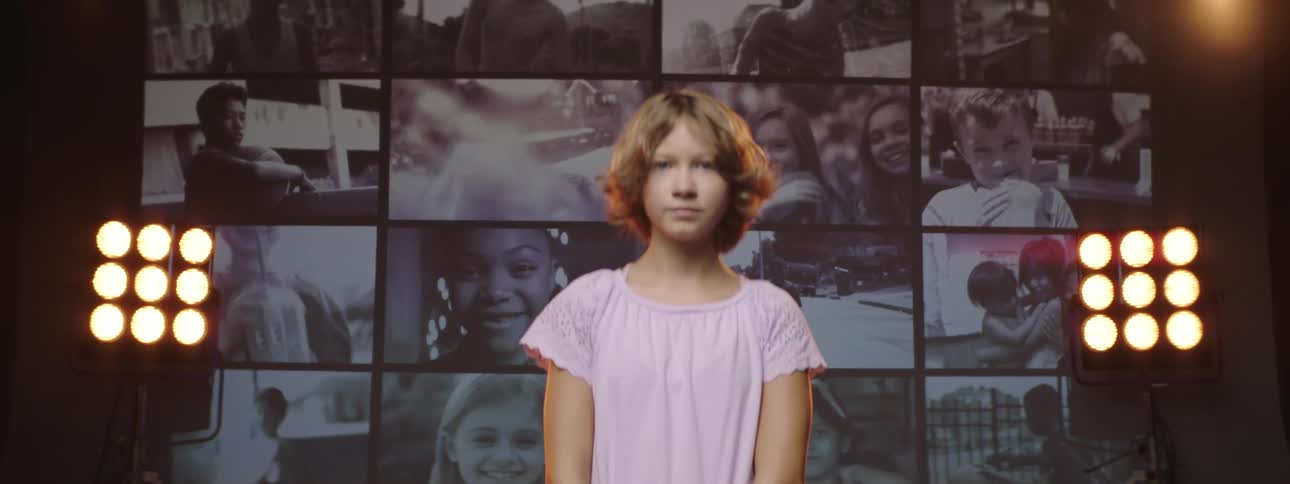 A girl turns around from watching a large screen playing multiple videos of children