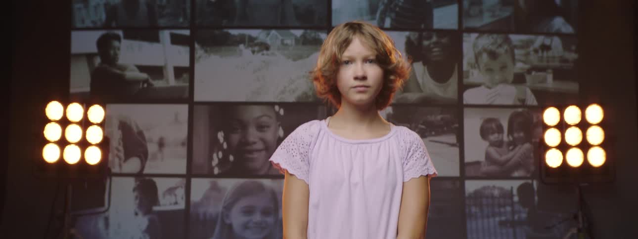 A girl turns back from a wall of screens playing video with stage lights glowing