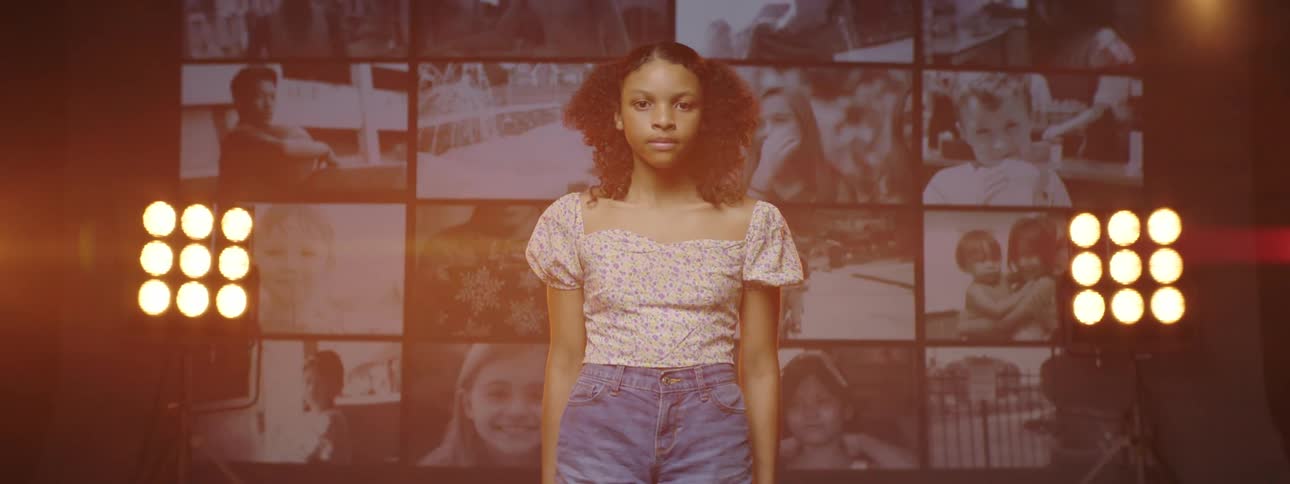 Girl standing on stage looking at the camera in front of a giant digital display