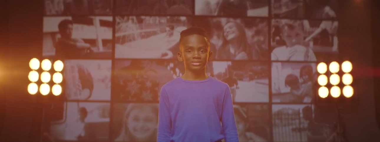 A boy smiles as he poses in front of a screen displaying a collage of videos
