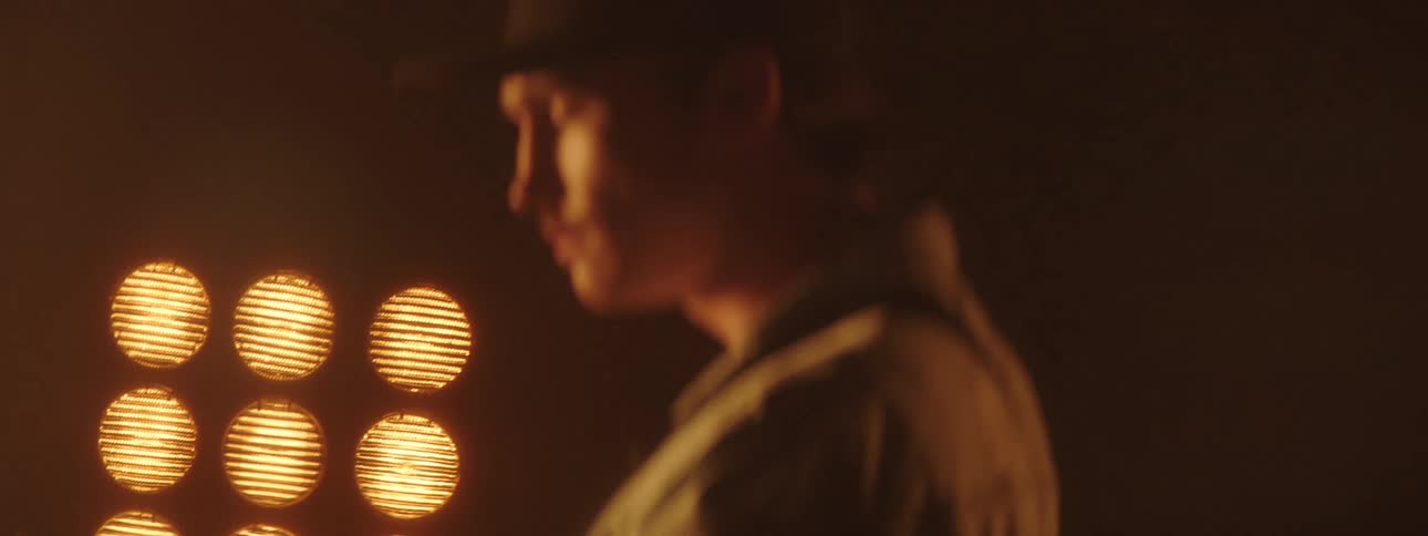 A man leans forward while playing the guitar in front of bright lights