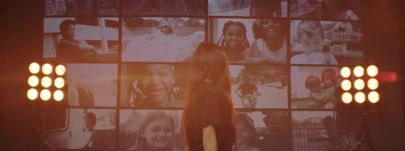 Young woman stands in front of series of screens showing the images of children