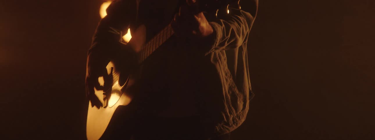 A guitarist plays his guitar before bright stage lights